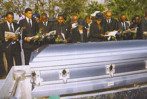 A group of people standing around a silver coffin