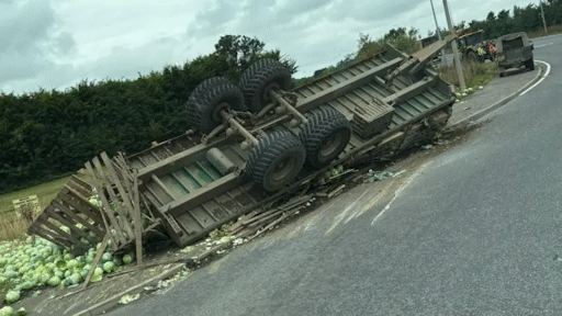 An overturned trailer with cabbages spilling into the road