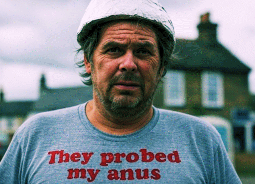 A man wearing a tinfoil helmet and a t-shirt that reads 'They probed my anus'