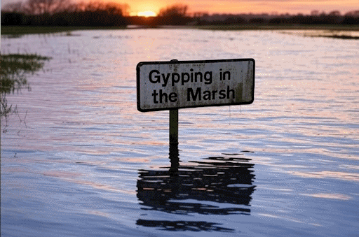 The sun setting over a flooded fenland landscape, with a sign reading Gypping in the Marsh sticking up through the floodwaters